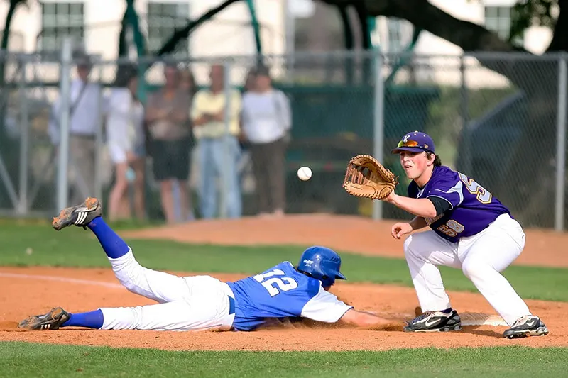A high school baseball pitcher mid-delivery from behind home plate.