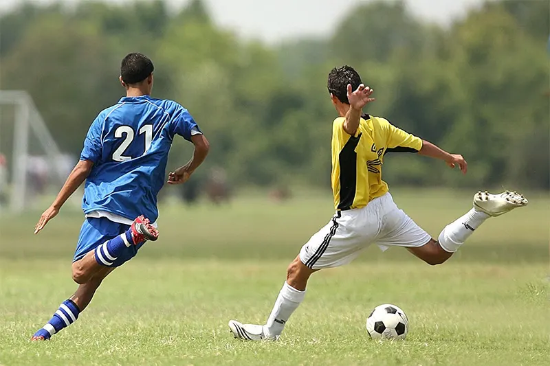 Two soccer players challenging for a loose ball at midfield.